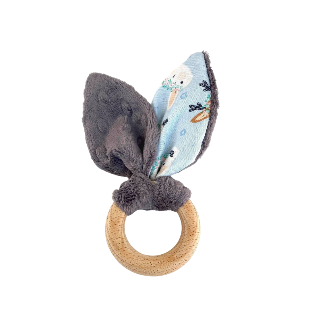 Hochet de dentition fait d’un anneau de bois et d’oreilles de lapin en minky gris foncé et tissus à motifs bleu pâle.